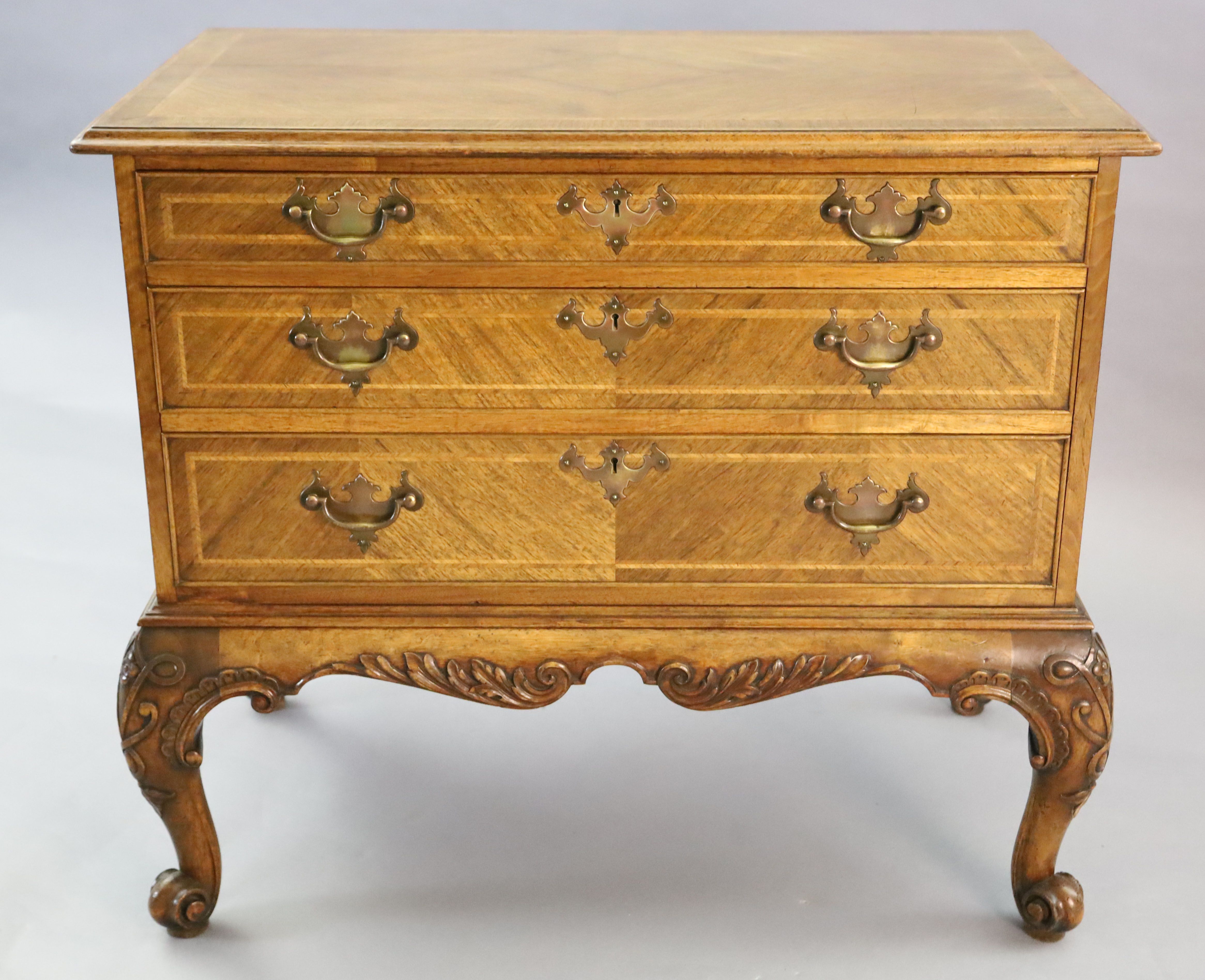 A Georgian style crossbanded walnut chest of three graduated long drawers, W.3ft 1in. D.1ft 10in. H.2ft 8in.